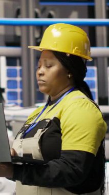 Çevre dostu endüstriyel santraldeki dikey video teknisyeni defter kullanarak üretim ekipmanlarını izliyor ve arızaları teşhis ediyor. Fabrika çalışanı güneş panelleri montajındaki onarım görevlerini koordine ediyor