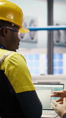 Dikey video Akıllı güneş panelleri fabrika mühendisliği ekibi dizüstü bilgisayarla üretim hatlarını denetliyor. Takım çalışması sektörü 4.0 fabrika çalışanları makinelerin en uygun verimlilikte çalışmasını sağlar