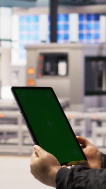 Fabrikada mühendis tarafından IoT sensör verilerini analiz etmek için kullanılan yeşil ekran tabletinin dikey görüntüsü. Renkli anahtar kullanarak fotovoltaik sistemleri yöneten endüstriyel fabrika işçisi