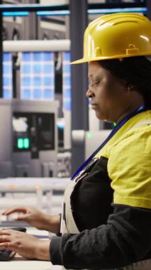 Akıllı fabrika uzmanındaki dikey videolu kadın otomatik iş akışlarını uygulamak için bilgisayarı kullanır. Endüstri 4.0 fabrikasında PC kullanan Afrikalı Amerikalı teknisyen sensörleri üretime entegre etmek için kamera A 'yı kullanıyor.