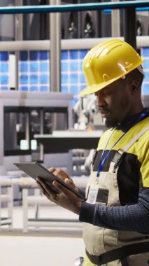 Dikey video akıllı fabrika uzmanı otomatik sistemleri test ediyor, operasyonel bütünlüğü izliyor. Endüstri 4.0 tesis teknisyeni hasar tespiti ve onarım ekipmanları, kamera A