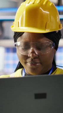 Dikey video gülümseyen akıllı fabrika mühendisi dizüstü bilgisayarda yazıyor, üretim hatlarının izlenmesini denetliyor. Sektör 4.0 fabrikasındaki neşeli kadın makinelerin en uygun verimlilikte çalışmasını sağlıyor.