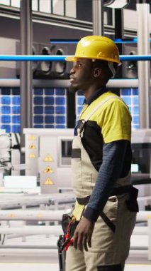 Dikey video mühendisi akıllı güneş enerjisi üretim tesisinde yürüyor, alet kutusuyla yüksek teknoloji makinelerini ayarlıyor. Afrikalı Amerikalı sorun çıkaran adam fotovoltaik montaj ekipmanı, kamera A