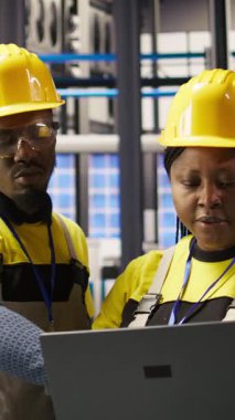 Dikey video mühendislik ekibi yüksek teknoloji makinelerini ayarlamak ve sensör verilerini analiz etmek için dizüstü bilgisayar kullanıyor. İş yerindeki ekip çalışanları montaj ekipmanları, kamera A