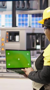 Fotovoltaik fabrikasında sistem performans ölçümlerine bakmak için krom anahtar dizüstü bilgisayar kullanan dikey video mühendisi. Sektör 4.0 santralinde çalışan işçiler enerjiyi izlemek için yeşil ekran modelleme defteri kullanıyorlar