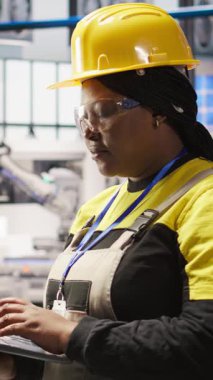 Dikey video akıllı fabrika uzmanı dizüstü bilgisayarda daktilo kullanıyor, güvenilirliğini sağlamak için otomatik sistemleri test ediyor. Sanayi 4.0 fabrika teknisyeni, darboğazları belirlemek ve optimize etmek için dizüstü bilgisayar kullanıyor