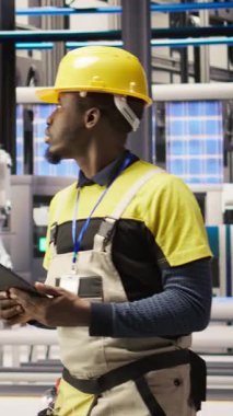 Teçhizatı değiştirmeden önce IoT sensörlerini analiz etmek için tablet kullanan dikey video akıllı fabrika teknisyeni. Endüstri 4.0 'daki Afrikalı Amerikalı adam dinlenme süresini azaltmak için sistem kontrolü yapıyor.