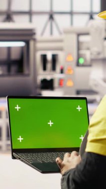 Dikey video fabrikası mühendisi yeşil ekran dizüstü bilgisayarda yazarak üretim hatlarını izliyor. Sektör 4.0 fabrikasındaki kadın, makinelerin krom anahtar modellemesi kullanarak en uygun verimlilikte çalışmasını sağlıyor.