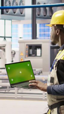 Dikey video güneş panelleri fabrika mühendisi vites arızalarını tahmin etmek için performans verilerini yeşil ekran laptopuyla analiz eder. Fotovoltaik fabrika işçisi bakım için model defter kullanıyor