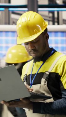 Güneş panelleri fabrikasındaki dikey video teknisyeni dizüstü bilgisayar kullanarak robot montaj hatlarını denetliyor ve kalite kontrolü sağlıyor. Endüstriyel fabrika işçisi otomatik taşıma sistemlerini not defteri kullanarak izliyor