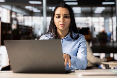 Kendine güvenen Hintli genel müdür, bir dizüstü bilgisayar ve belgelerle iş ve operasyonları çözmek için masasında çoklu görev yapıyor, son teslim tarihlerini karşılarken stratejik kararlar veriyor..