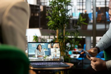 Yönetici evden çalışan işbirlikçilerle konuşuyor, video konferans yapıyor, dizüstü bilgisayarla yeni müşteri görevlendirme projesini sunuyor. Ekip lideri internet video çağrısında işçilerle konuşuyor