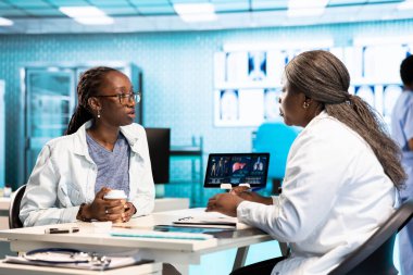 Bir hastayla tıbbi verileri inceleyen kadın pratisyen, sağlığa odaklı uzman istişare sırasında etkileşimi ve güveni teşvik eden. Afrikalı Amerikalı kız tavsiye istiyor..