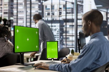 İş adamı, yeşil ekranlı cihazlarla iş istasyonunda oturmuş, işletme büyümesi için idari görevler üzerinde çalışıyor. Proje hedeflerini desteklemek için performans ölçümleri geliştiriliyor.