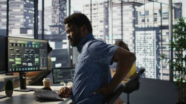 Yüzü asık bir çalışan, hatayı düzeltmek için kod incelemesi yaparken kas gerginliğini azaltmak için esniyor. Ofisteki yorgun personel kötü duruş, optimizasyon kodu ve kamera B yüzünden sırt ağrısı çekiyor.