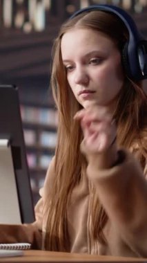 Dikey Video Genç kadın yetişkin terapi müziği dinliyor ve üniversite kütüphanesinde odaklanması için ortam seslerini kullanıyor. Öğrenci akademik araştırma yapıyor. Kamera.