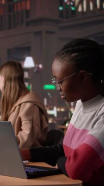 Dikey Video Üniversitesi öğrencisi kampüs kütüphanesinde bir arkadaşıyla el yazısı notlarını tamamlamak için sınav hazırlığı yapıyor. Veritabanından bilgi paylaşan kızlar. Kamera.