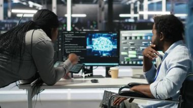 Tekerlekli sandalyedeki yönetici ve veri merkezindeki iş arkadaşı, kapatma süresini en aza indirmek için yapay zeka ağacı yazılımı kullanıyor. Sunucu merkezi engelli bilişim uzmanı ve iş arkadaşı görsel programlama uygulaması kullanarak, kamera B