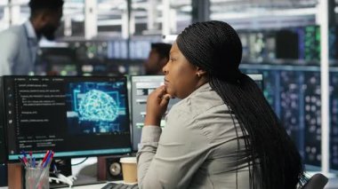 Veri merkezi çalışanı veri tabanlarını analiz etmek için yapay zeka algoritmaları kullanıyor. Sunucu odasında yapay zeka sinirsel ağlar kullanan Afrikalı Amerikalı bir kadın var.