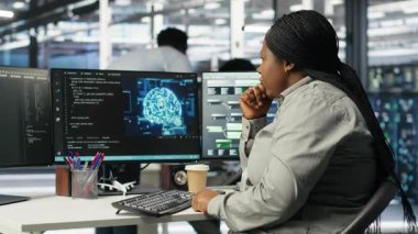 Veri merkezi teknisyeni donanımı yapılandırmak için yapay zeka derin öğrenme modelleri kullanıyor. Afro-Amerikalı kadın sunucu odasında yapay zeka programlama dili üzerinde çalışıyor, sistem optimizasyonu, kamera B