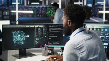 Sunucu çiftliği bilgisayar bilimcisi yapay zeka veri analizi grafiklerini yorumluyor. Veri merkezindeki Afrikalı Amerikalı adam yapay zeka programı kullanarak öngörü sistemi ölçümleri ve kamera A 'yı gösteriyor.