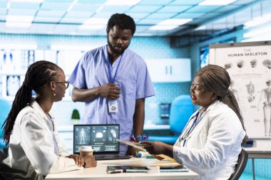 Siyahi bir kız, tıbbi kabinedeki pratisyen hekimle görüşüyor. Kişisel bakım için MR ve röntgen analizini tartışıyor. Sıhhiye tarama yorumu sırasında sağIık ve rehberlik sunar.