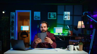 Teknoloji uzmanı, düşük bütçeli tableti ilgili izleyicilere stüdyoda sunuyor. İnternet izleyicisi önünde dijital aygıtı inceleyen viral içerik yaratıcısı, kamera B