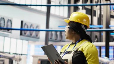 Akıllı fabrikadaki gülümseyen mühendis tablet kullanarak tahmin yürüterek IoT sensör verilerini analiz ediyor. Fotovoltaik sistemlerin işlevsel güvenilirliğini yöneten endüstriyel fabrika işçisi, kamera B