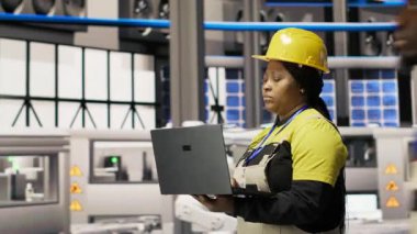 Çevre dostu sanayi fabrikasındaki teknisyen, üretim ekipmanlarını not defteri kullanarak izliyor ve arızaları teşhis ediyor. Fabrika çalışanı güneş panelleri montaj hattındaki tamir görevlerini koordine ediyor, kamera B