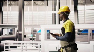 Elinde tablet tutan bir görevli fabrikada yürüyor, sistemleri denetliyor, ekipmanların en uygun verimlilikte çalışmasını sağlıyor. Sanayi fabrikası elektrikçisi tesis altyapısını denetliyor, kamera A