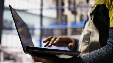 Otomatik sistemleri test etmek, üretim ölçümlerini izlemek için dizüstü bilgisayar kullanan akıllı fabrika işçilerini kapatın. Endüstri 4.0 tesis uzmanı, arızaları tespit etmek ve düzeltmek için makineleri inceliyor, kamera A