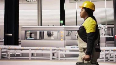 Endüstriyel fabrikada yürüyen teknisyenler, ekipman hatalarını teşhis etmek ve düzeltmek için alet kutusunu kullanıyorlar. Üretim fabrikasındaki Afrikalı Amerikalı kadın koordinatları montaj hatlarındaki tamir görevleri, kamera A