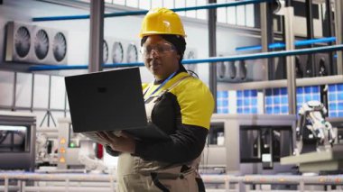 Güneş panelleri fabrika teknisyeni sistemleri denetlemek için dizüstü bilgisayar kullanır, makinelerin en uygun verimlilikte çalışmasını sağlar. Fotovoltaik fabrikası çalışanı işlemleri devam ettirmek için deftere yazılım kullanıyor, kamera A