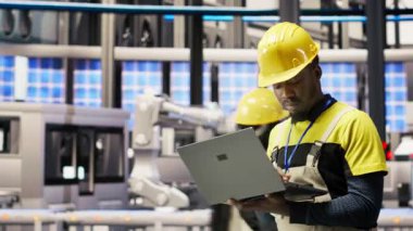 Güneş panelleri fabrikasındaki teknisyen dizüstü bilgisayar kullanarak robot montaj hatlarını denetliyor, kalite kontrolü sağlıyor. Endüstriyel fabrika işçisi otomatik taşıma sistemlerini not defteri, kamera B kullanarak izliyor.