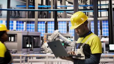 Güneş panelleri fabrikasındaki teknisyen dizüstü bilgisayar kullanarak robot montaj hatlarını denetliyor, kalite kontrolü sağlıyor. Endüstriyel fabrika işçisi otomatik taşıma sistemlerini not defteri, kamera A kullanarak izliyor.