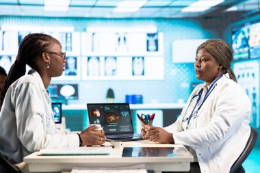 Afrika kökenli Amerikalı bir hasta tıbbi kabinede bir doktorla görüşüyor, kişisel bakım veya tedavi için teşhis raporlarını ve analizleri tartışıyor. Sağlık için tavsiye sunuyor..