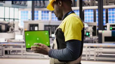 Mühendis yeşil ekran dizüstü bilgisayar kullanarak güneş paneli üretim hattı ekipmanlarını denetliyor. İşçi otomatikleştirilmiş sanayi 4.0 fabrikasında krom anahtar not defteri, kamera A kullanarak fotovoltaik montaj sistemi kuruyor.