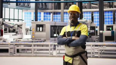 Güneş paneli üretim hattı ekipmanlarını denetleyen teknisyen portresi. Otomatik sanayi 4.0 fabrikasında bilgisayar ve kamera A kullanarak fotovoltaik montaj sistemleri sürdüren Afrikalı Amerikalı bir adam.