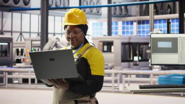 Gülümseyen akıllı fabrika mühendisi dizüstü bilgisayarda yazı yazıyor, üretim hatlarının izlenmesini denetliyor. Sektör 4.0 fabrikasındaki neşeli kadın makinelerin en uygun verimlilikte çalışmasını sağlar. Not defteri, kamera A 'yı kullanarak.