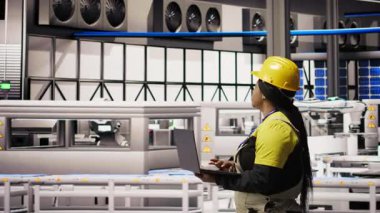 Çevre dostu sanayi fabrikasındaki teknisyen, üretim ekipmanlarını not defteri kullanarak izliyor ve arızaları teşhis ediyor. Fabrika çalışanı güneş panelleri montaj hattındaki tamir görevlerini koordine ediyor, kamera A