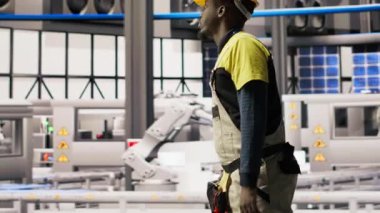 Akıllı güneş enerjisi üretim tesisinde yürüyen mühendis, yüksek teknoloji makinelerini kalibre etmek için alet çantası kullanıyor. Afrikalı Amerikalı sorun çıkaran adam fotovoltaik montaj ekipmanı, kamera B