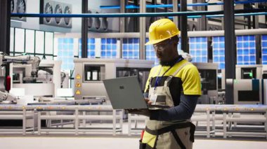 Güneş panelleri fabrikasındaki gülümseyen teknisyen portresi robot üretim hatlarını denetliyor, kalite kontrolü sağlıyor. Endüstriyel fabrikadaki Afrikalı Amerikalı adam otomatik taşıma sistemleri, kamera A 'yı izliyor.