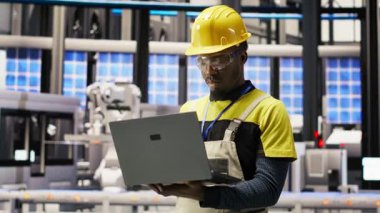 Güneş panelleri fabrikasındaki gülümseyen teknisyen portresi robot üretim hatlarını denetliyor, kalite kontrolü sağlıyor. Endüstriyel fabrikadaki Afrikalı Amerikalı adam otomatik taşıma sistemlerini izliyor, kamera B