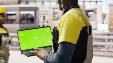 Güneş panelleri fabrika mühendisi vites arızalarını tahmin etmek için performans verilerini yeşil ekran laptopuyla analiz ediyor. Fotovoltaik fabrika işçisi bakım prosedürlerini takip etmek için B kamerasını kullanıyor.