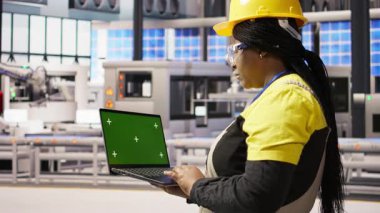 Endüstriyel fabrikadaki teknisyen ekipman hatalarını teşhis etmek için yeşil ekran dizüstü bilgisayar kullanıyor. Montaj hatlarındaki tamir görevlerini koordine etmek için krom anahtar maket defteri kullanan bir fabrika uzmanı, kamera A