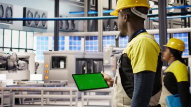Akıllı fabrikadaki mühendis, yeşil ekran tablet kullanarak kalite kontrolü sağlayan robot montaj hatlarını denetliyor. İşçi otomatik taşıma sistemlerini krom anahtar cihazı, kamera kullanarak izliyor.