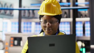 Gülümseyen akıllı fabrika mühendisi dizüstü bilgisayarda yazı yazıyor, üretim hatlarının izlenmesini denetliyor. Sektör 4.0 fabrikasındaki neşeli kadın, makinelerin en uygun verimlilikte çalışmasını sağlar. Not defteri, kamera B 'yi kullanarak.