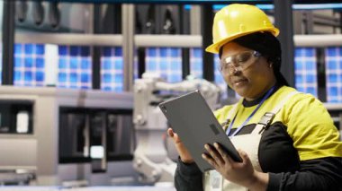 Güneş panellerinde çalışan kadın makine sistemlerini denetlemek için tablet kullanıyor. Afrikalı Amerikalı fotovoltaik fabrikası çalışanı işlemleri sürdürmek için yazılımı kullanıyor, kamera B