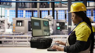 Akıllı bir fabrika uzmanı olan kadın otomatik iş akışlarını uygulamak için bilgisayar kullanır. Endüstri 4.0 fabrikasında PC kullanan Afrikalı Amerikalı teknisyen sensörleri üretime entegre etmek için kamera A 'yı kullanıyor.