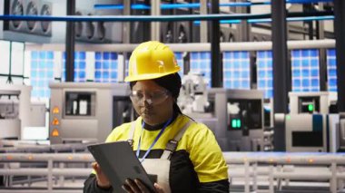 Güneş panellerinde çalışan kadın makine sistemlerini denetlemek için tablet kullanıyor. Afrika kökenli Amerikan fotovoltaik fabrikası çalışanı işlemleri sürdürmek için yazılımı kullanıyor, kamera A